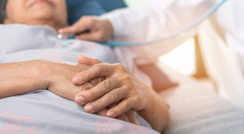 Hospitalized elderly patient woman laying on bed with cardiologist doctor or physician examining heart health, checking pulse in hospital clinic exam room