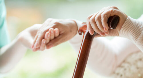 Elder person using wooden walking cane during rehabilitation in friendly hospital
